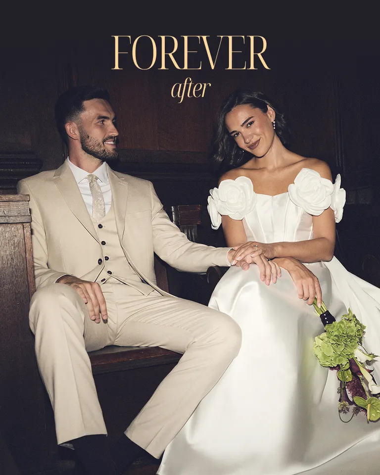 Bride in white floral off-shoulder gown and groom in beige suit seated together, "Forever After" wedding campaign